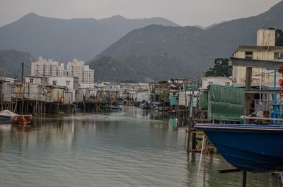 Boats moored in river by buildings against sky