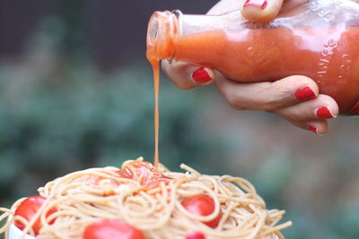 Cropped hand of woman pouring sauce on noodles