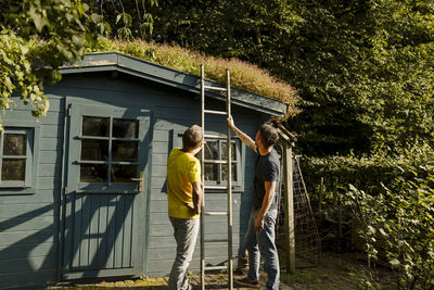 Father and son holding ladder in front of house