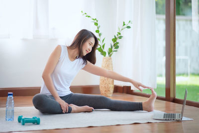 Full length of woman stretching while sitting at home