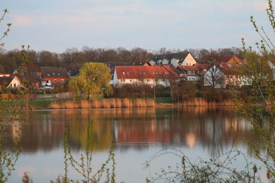 Houses by lake and buildings against sky