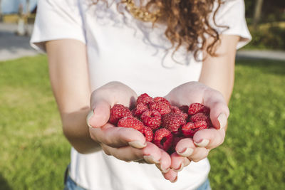 Young woman holding fresh raspberries at park during sunny day