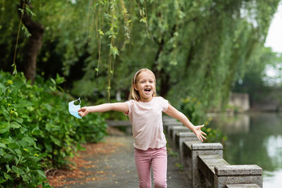 Cheerful girl holding mask running by canal