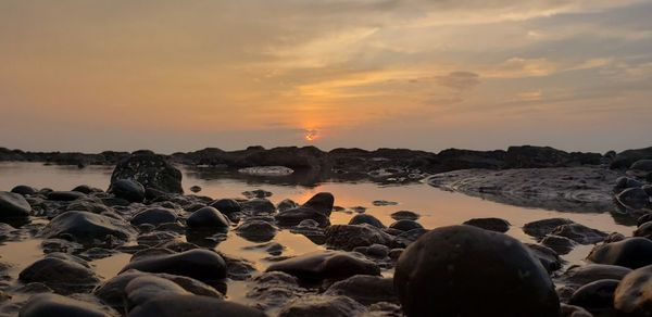 Rocks on beach against sky during sunset