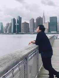 Profile view of young man standing on pier over river in city