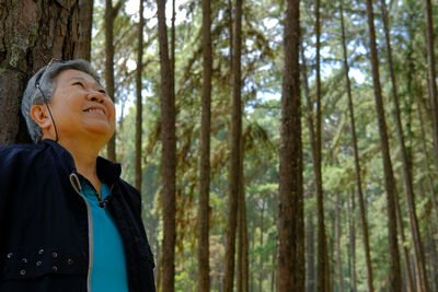 Smiling senior man standing by tree trunk in forest