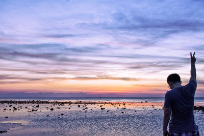 Rear view of silhouette man photographing on beach against sky