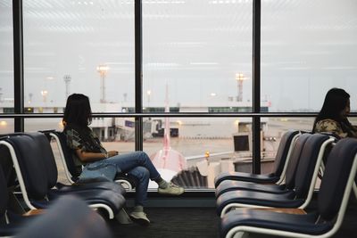 Women sitting on chairs at airport departure area