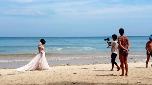 Friends enjoying at beach against sky