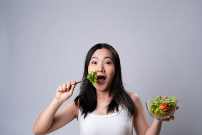 Portrait of young woman eating food against white background