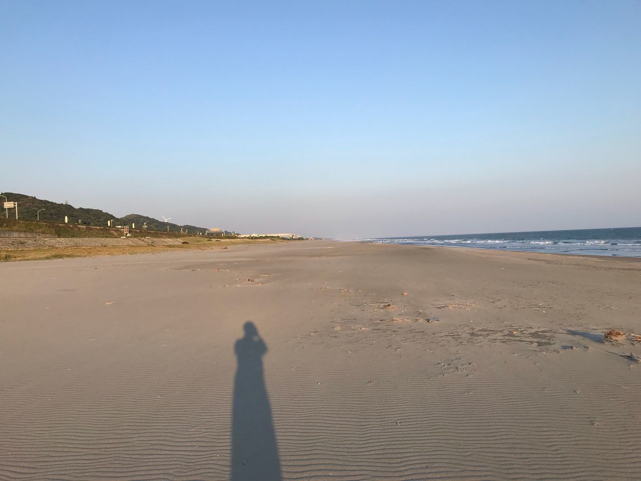 beach, sand, nature, sea, real people, scenics, shadow, outdoors, beauty in nature, sunlight, clear sky, tranquil scene, copy space, tranquility, day, one person, water, arid climate, sand dune, standing, vacations, lifestyles, horizon over water, sky, men, people