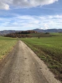 Dirt road amidst field against sky