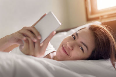 Portrait of woman using phone while relaxing on bed at home