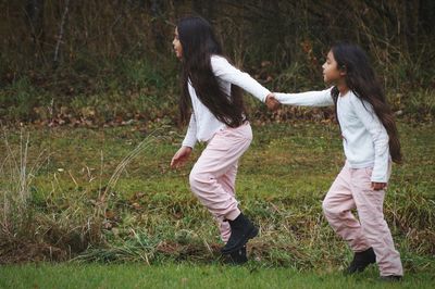 Full length of sisters walking on grassy field