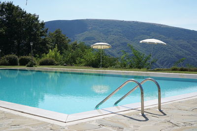 Swimming pool by trees against sky