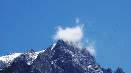 Low angle view of snowcapped mountains against blue sky