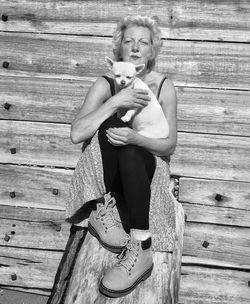 Portrait of woman with puppy sitting against wooden wall