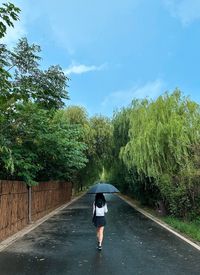 Rear view of woman walking on road against trees