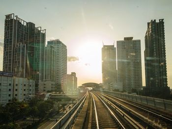 Railroad tracks amidst buildings in city against bright sky