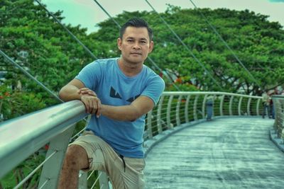 Portrait of man standing by railing against trees