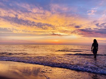 Woman wading in sea against cloudy sky during sunset