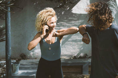 Smiling woman giving elbow bump to man while talking on mobile phone outdoors