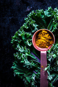 Top down view of fresh kale and curry powder in a copper spoon on dark surface
