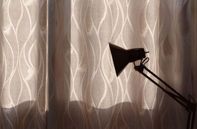 Close-up of electrical lampshade against bright curtains 