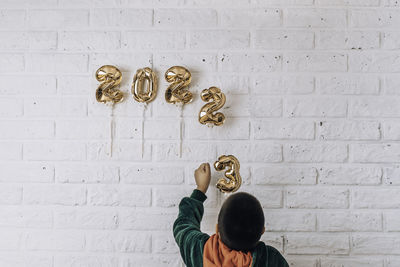 Little boy decorates the wall of the house with golden numbers 2023. change numbers