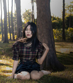 Portrait of young woman sitting on tree trunk in forest