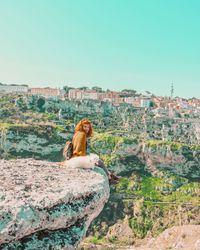 View of man sitting on rock against clear sky