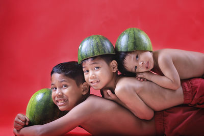 Portrait of shirtless boys with watermelons lying against red background