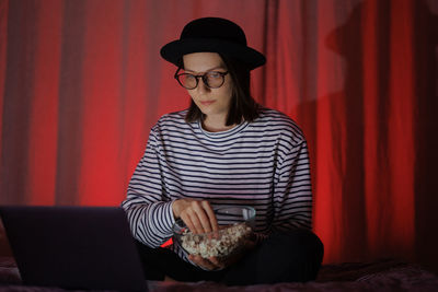 Portrait of young woman sitting on sofa at red curtain