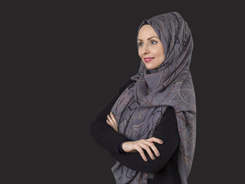 Smiling woman wearing hijab while standing against black background