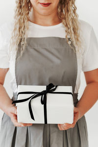 Midsection of woman holding book while standing against white background