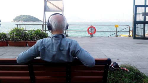 Rear view of woman sitting on railing against sea