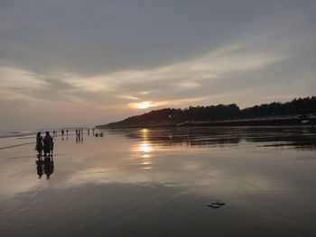 Silhouette of tourists in water at sunset