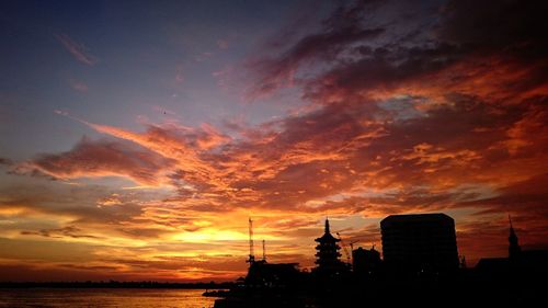 Silhouette of city against cloudy sky during sunset