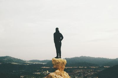 Rear view of man standing on rock against sky