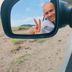 Smiling man on side-view mirror against sky