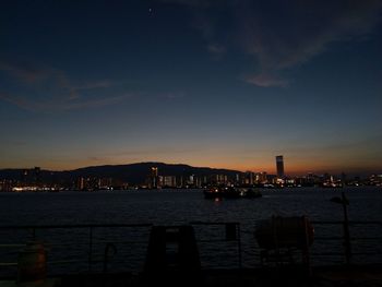 Illuminated buildings by river against sky at sunset