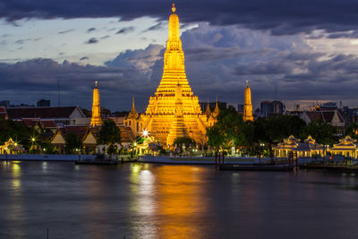 Illuminated temple building by river against sky in city