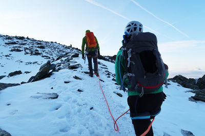 Low angle view of people hiking on snowcapped mountain against sky