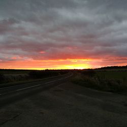 Road by agricultural field against sky during sunset