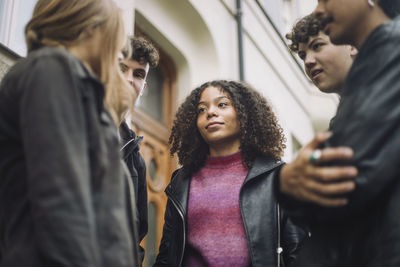 Low angle view of teenage girl discussing with male and female friends at street