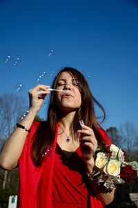 Beautiful woman blowing bubbles against clear blue sky