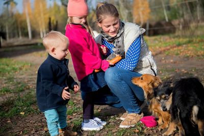 Happy family-mother with  children hugging and feeds pets dogs, cats and goats in countryside farm