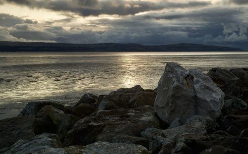Rocks on beach against sky during sunset