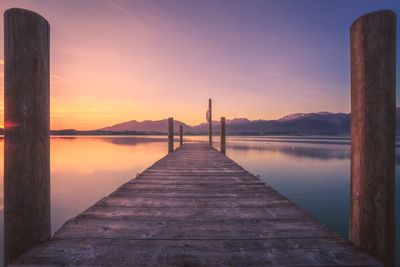 Pier on calm lake against orange sky