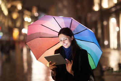 Smiling woman using digital tablet while standing in city during rainy season